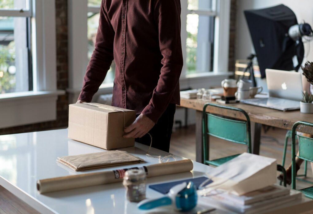 Seseorang menyiapkan kotak paket di atas meja untuk barang yang akan dijual online